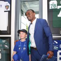 Guest posing with a child in front of four framed jerseys at the Jamie Hosford Football Center dedication.